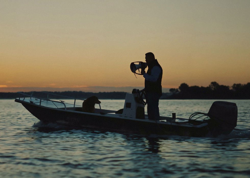 Guy Monseair with his dog in a motor boat at dusk coaching rowing team