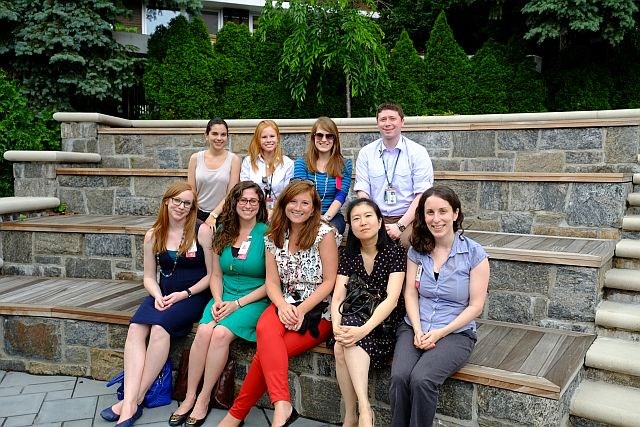 A group of psychiatry students dressed in business causual clothing sit on a stone bench.